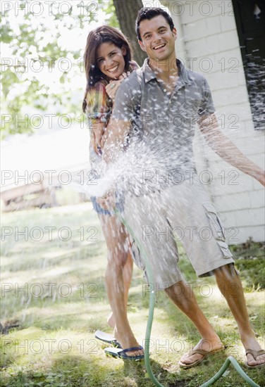 Portrait of couple spraying hose in backyard. Date: 2008