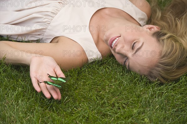 Woman laying on grass holding green butterfly.