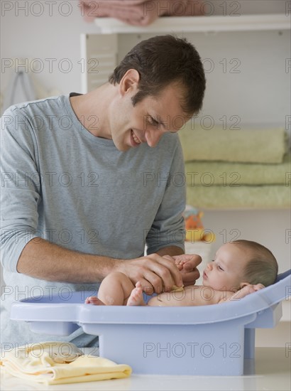 Father bathing baby son in baby bathtub.