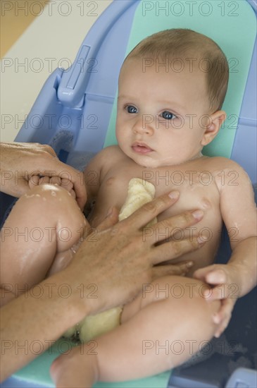 Mother bathing baby son in baby bathtub.