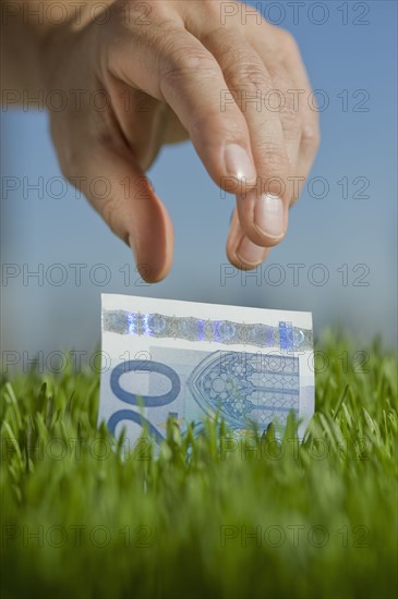 Close up of hand reaching for twenty euro bill.