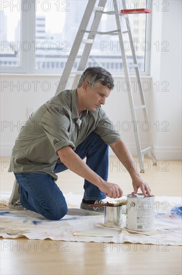 Man opening paint cans on drop cloth.