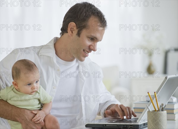Father working on laptop and holding son.