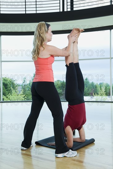 Yoga instructor helping woman with headstand pose. Date : 2008