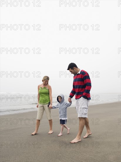 Parents holding hands with son on beach. Date : 2008