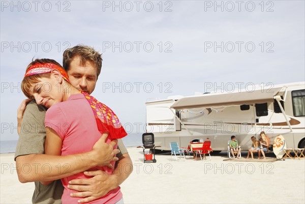 Couple hugging on beach with motor home in background. Date : 2008