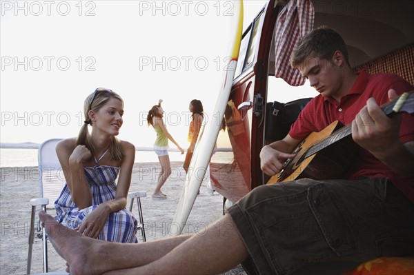 Man playing guitar in van on beach. Date : 2008
