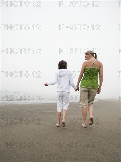 Mother and daughter holding hands and walking on beach. Date : 2008