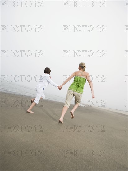 Mother and daughter holding hands and running on beach. Date : 2008