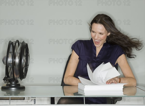 Fan blowing stack of papers at businesswoman’s desk.