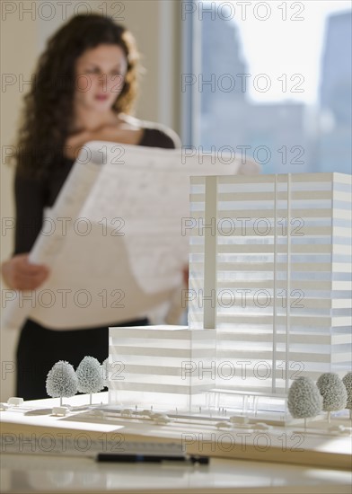 Architect viewing blueprints near building model.