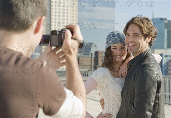 Man taking video of couple with city in background.