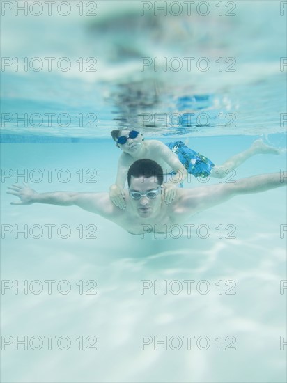 Boy swimming on father’s back underwater. Date : 2008