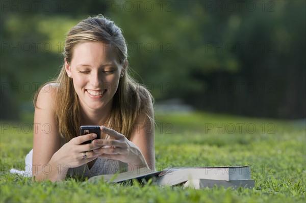 College student reading in grass and text messaging. Date : 2008