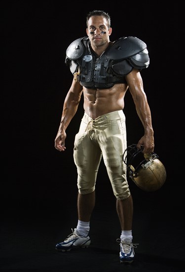 Football player wearing protective gear and holding helmet. Date : 2008