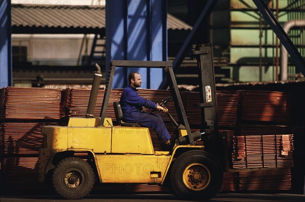 Worker lifting pallets of copper pipes on forklift. Date : 2008