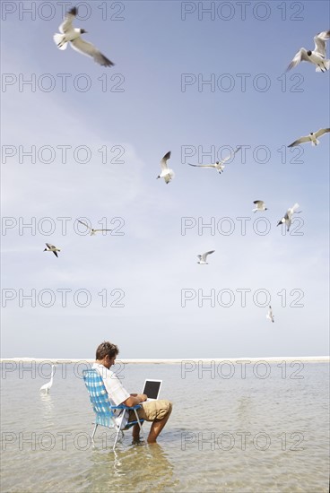 Man sitting in ocean surf with laptop. Date : 2008