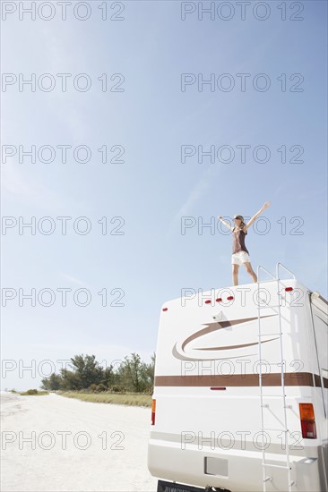 Woman standing on motor home with arms outstretched. Date: 2008