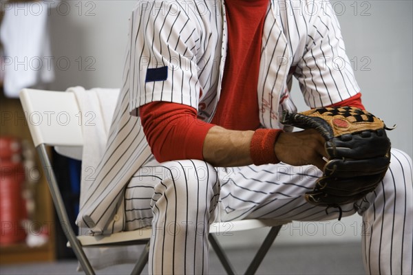 Baseball player holding glove in locker room. Date: 2008