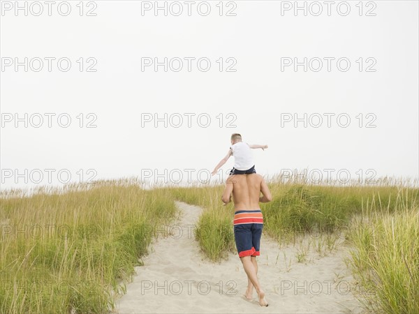 Father carrying son on shoulders at beach. Date: 2008