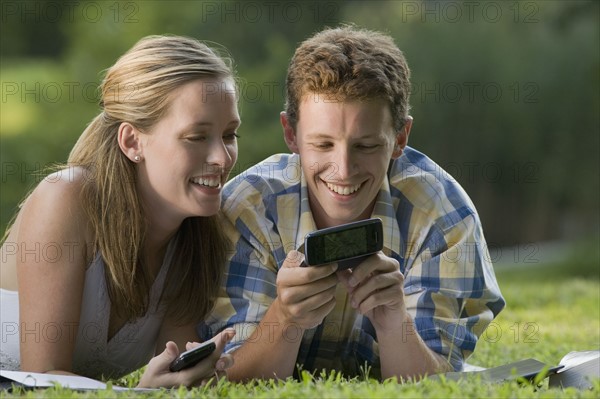 College students laying in grass with books and cell phones. Date : 2008