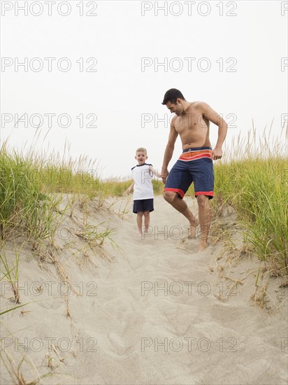 Father and son holding hands and running on beach. Date : 2008