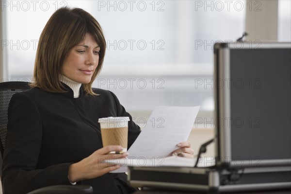 Businesswoman holding coffee and reading paperwork.