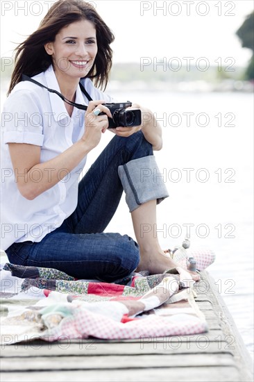 Woman with camera sitting on dock. Date: 2008