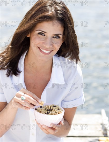 Portrait of woman eating granola on dock. Date: 2008