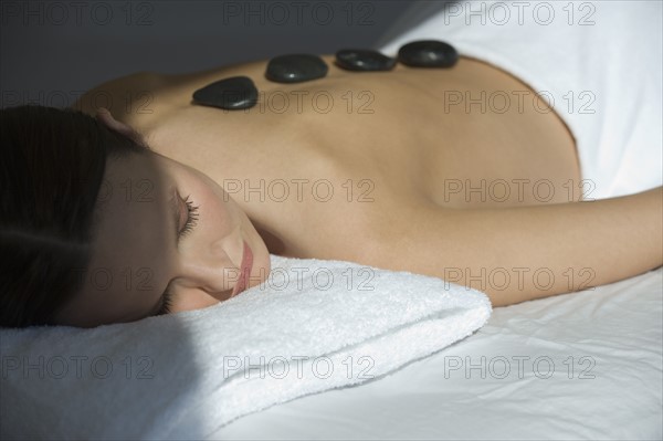 Woman laying on massage table with warm stones on back.