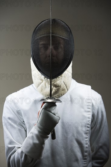 Portrait of fencer in uniform and mask holding fencing foil. Date: 2008