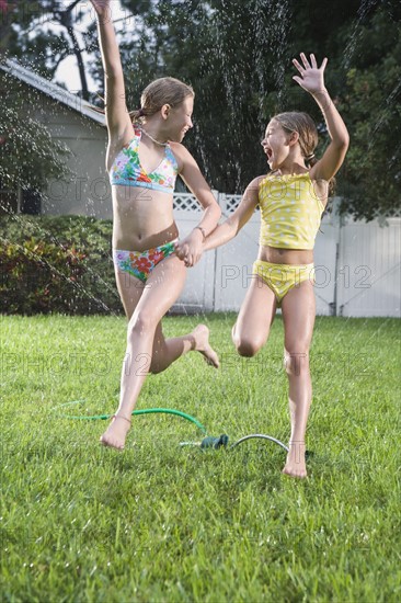 Sisters in bathing suits running through sprinkler. Date : 2008