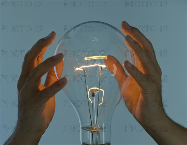 Hands cupped around large light bulb.