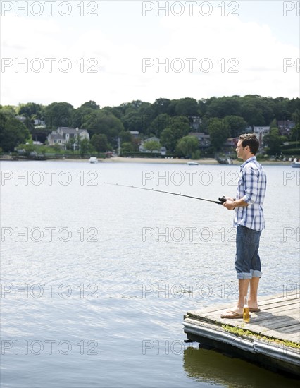 Man fishing off dock with beer at feet. Date : 2008