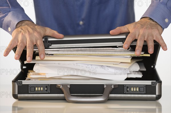 Businessman trying to close briefcase.