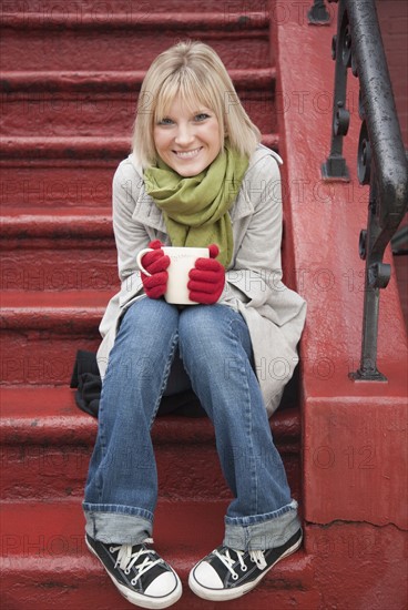 Woman drinking hot chocolate on front stoop. Photographe : Jamie Grill