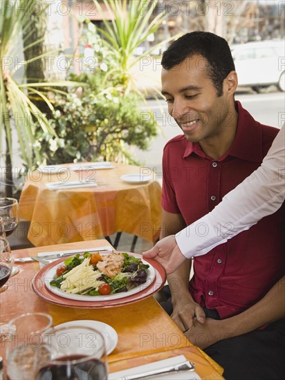 Waiter serving food to man in restaurant.