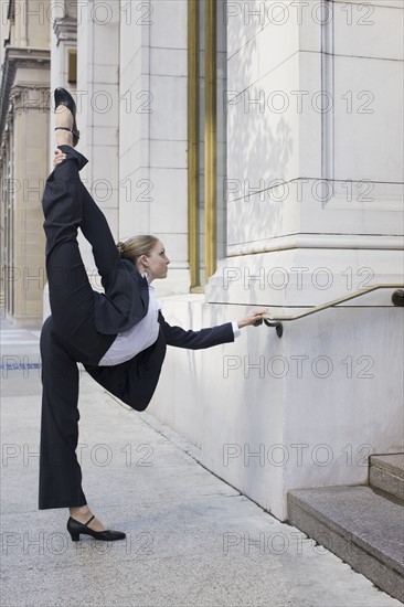 Businesswoman stretching on urban sidewalk. Photographe : PT Images