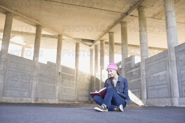 Young woman reading in urban setting. Photographe : PT Images