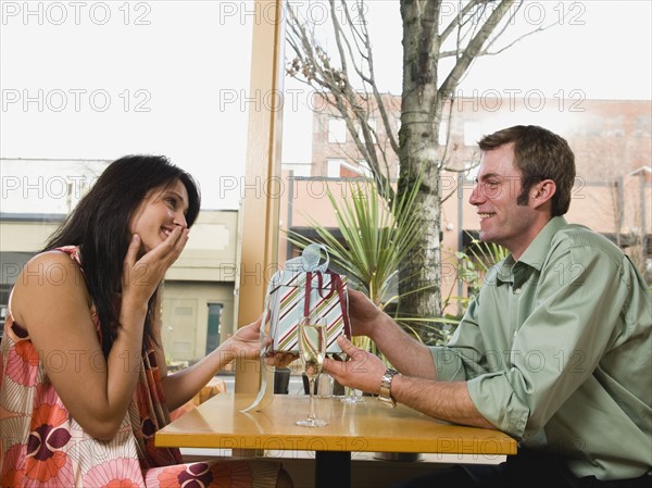 Man giving woman gift in restaurant.