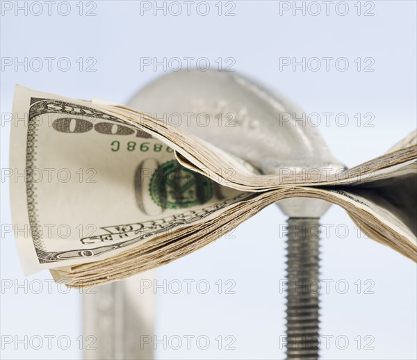 Paper currency squeezed in C clamp. Photographe : Jamie Grill
