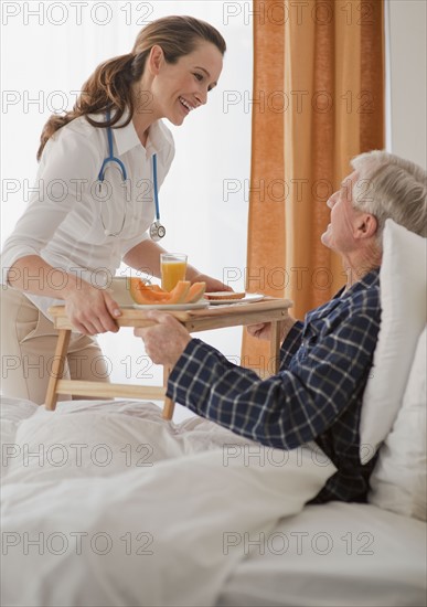 Nurse giving senior man breakfast.