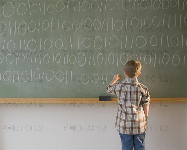 Boy writing binary code on blackboard.