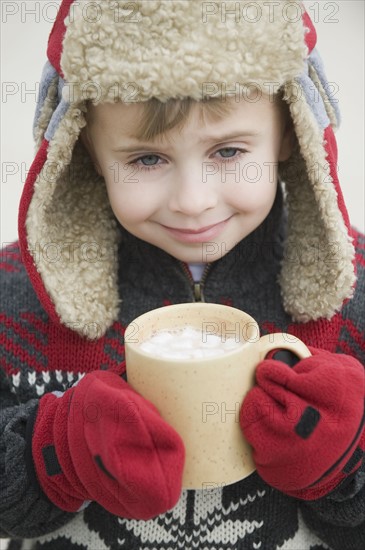 Boy in warm hat drinking hot chocolate.