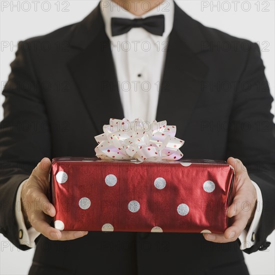 Man in tuxedo holding gift.