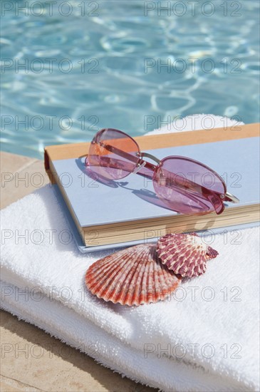 Book and sunglasses by swimming pool.