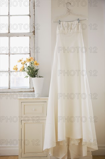 Wedding dress hanging in bed room. Photographe : Jamie Grill