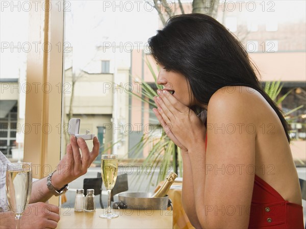 Man giving girlfriend engagement ring in restaurant.