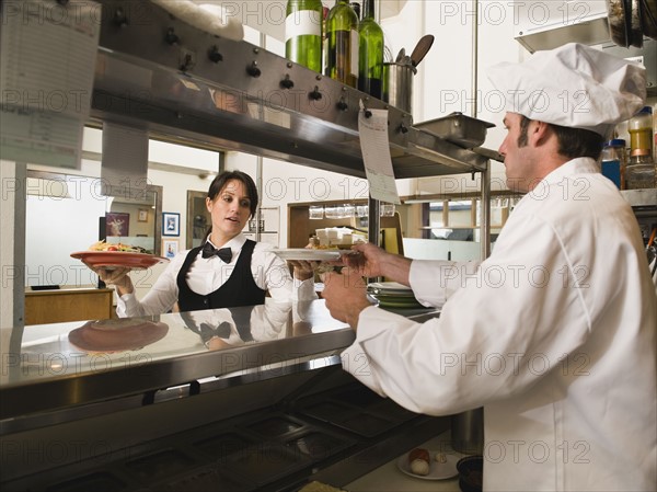 Chef giving waitress plates of food.