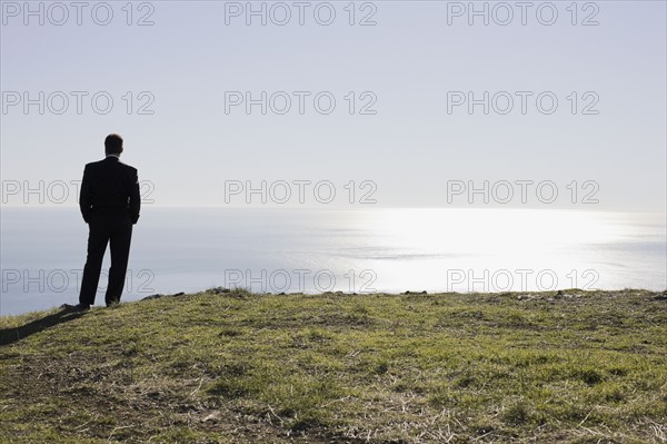 Businessman looking toward ocean. Photographe : PT Images